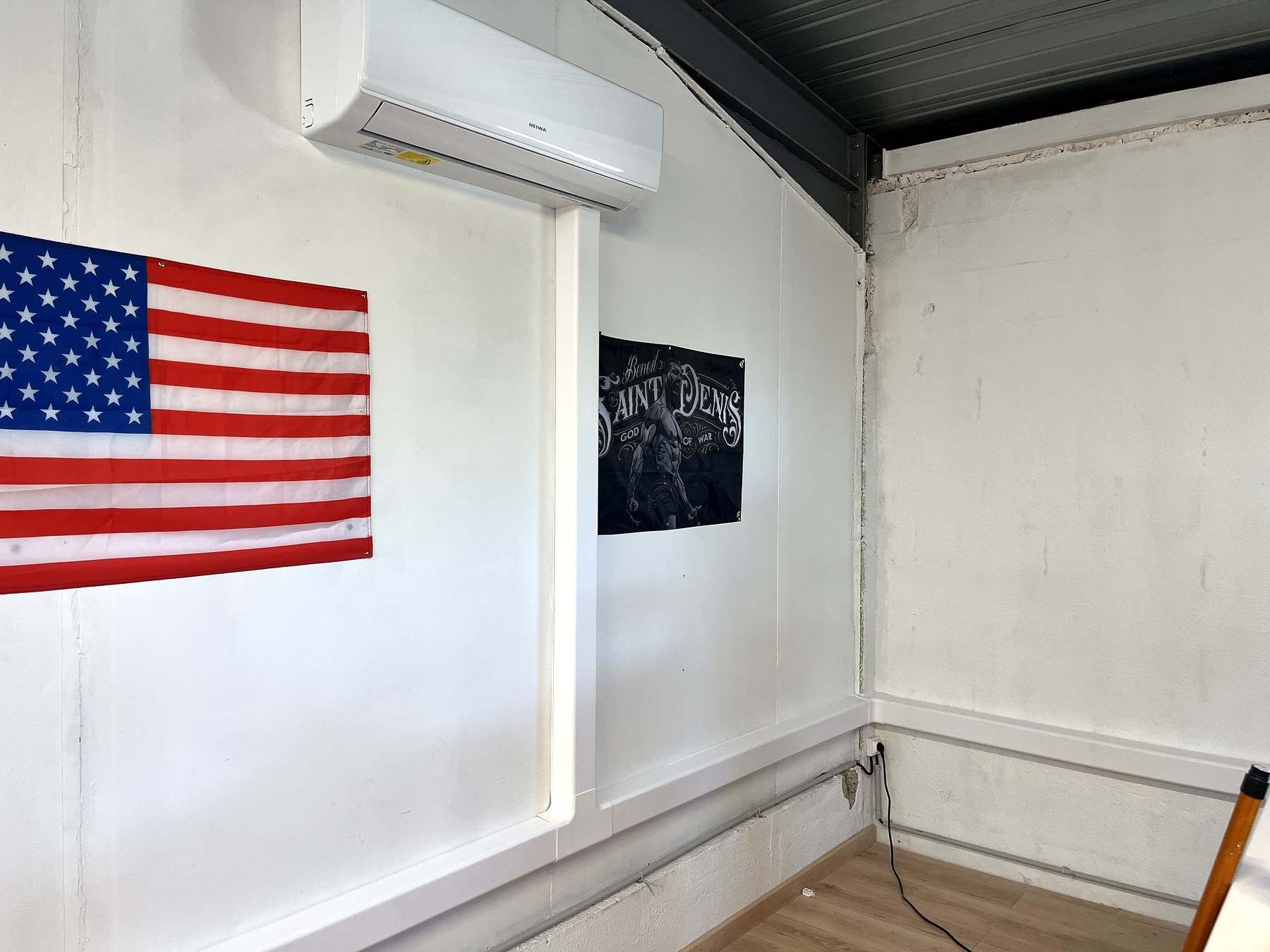 Unité murale Heiwa posée en haut d’un mur blanc, sa goulotte descendant verticalement jusqu’à la plinthe, à côté d’un drapeau américain.