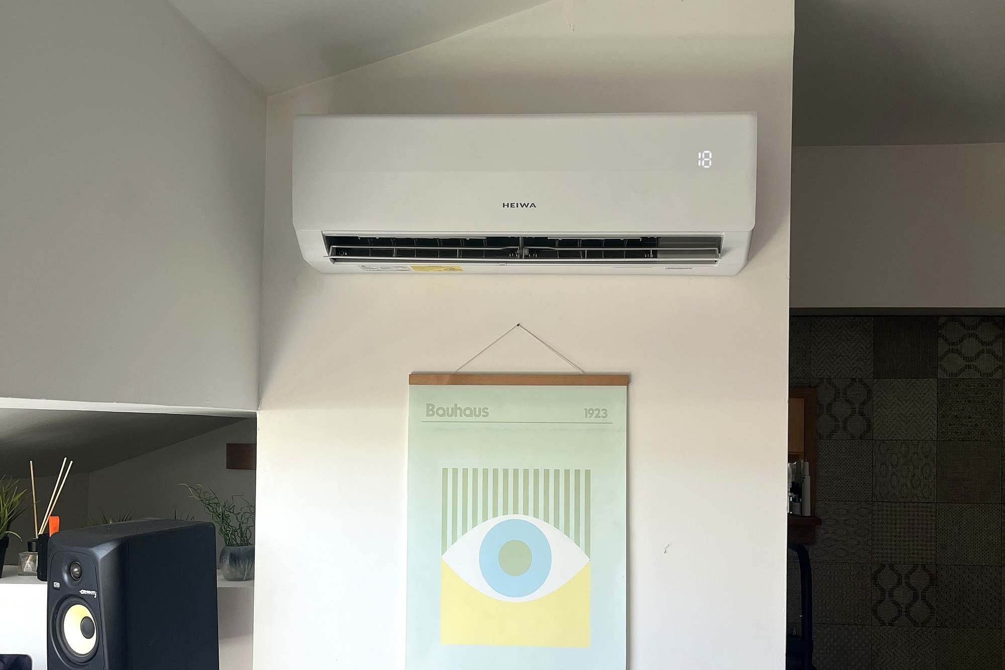 Unité murale Heiwa posée en haut d’un mur blanc dans un bureau, au-dessus d’une affiche encadrée, à côté d’une enceinte de studio.