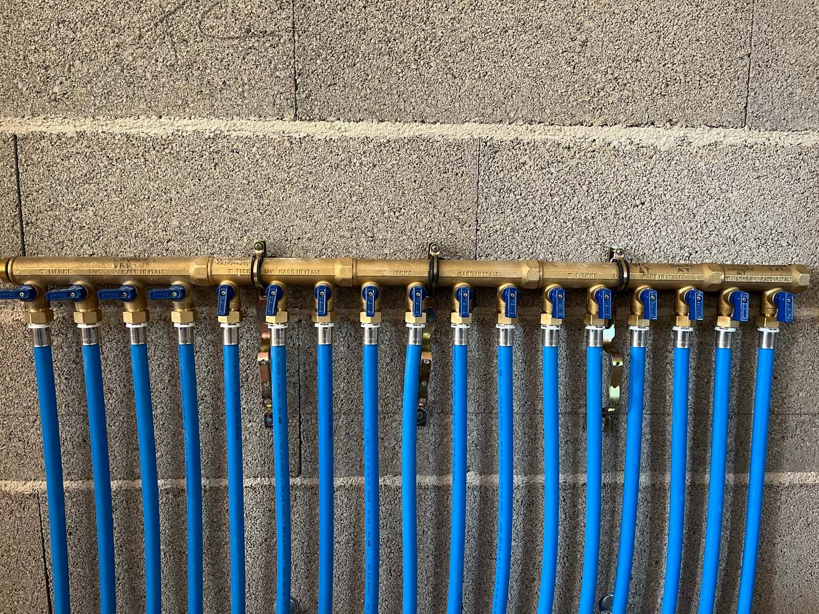 Nourrice de distribution en laiton alimentant une vingtaine de circuits en tube PER bleu, chaque départ équipé de sa vanne quart de tour et repéré au feutre.