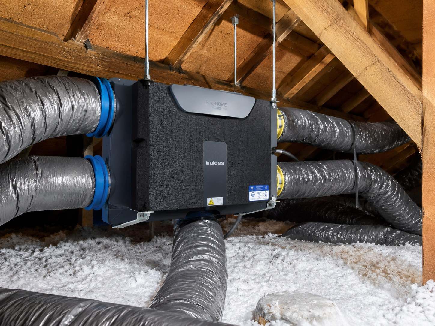 Caisson de VMC double flux Aldes EasyHOME suspendu sous charpente dans des combles isolés, raccordé à six gaines souples calorifugées.